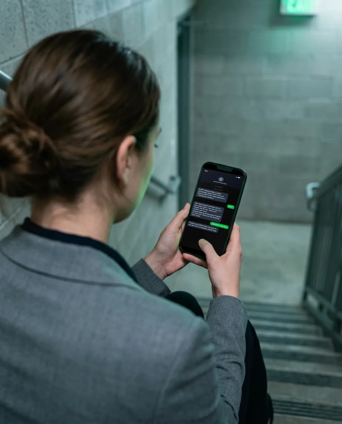 An office worker sitting in a stairwell types a HELP reply to an alert on her phone.